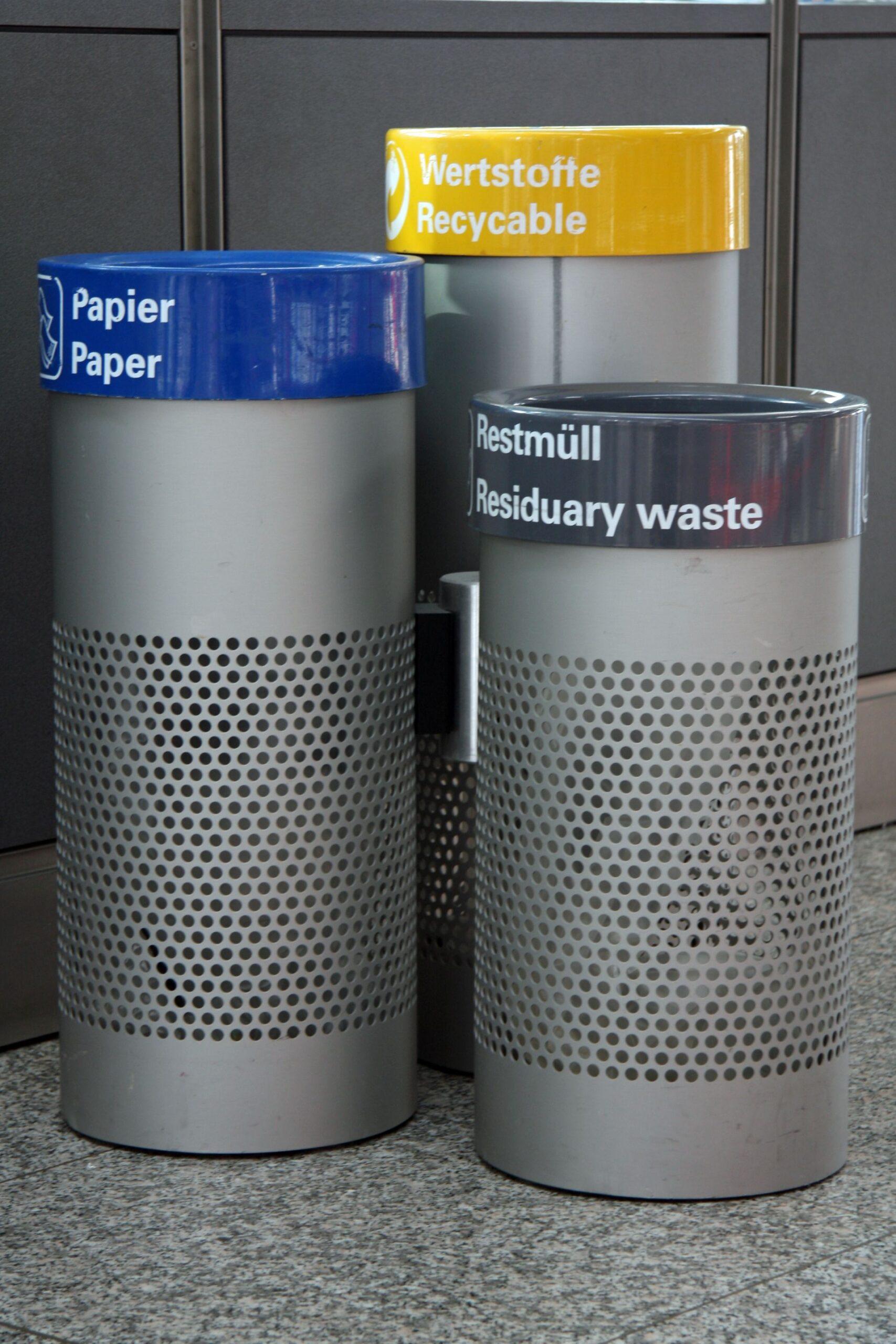 Drei beschriftete Abfallbehaelter zur Muelltrennung für Papier, Wertstoffe und Restmuell – aufgestellt in einer modernen Innenumgebung.