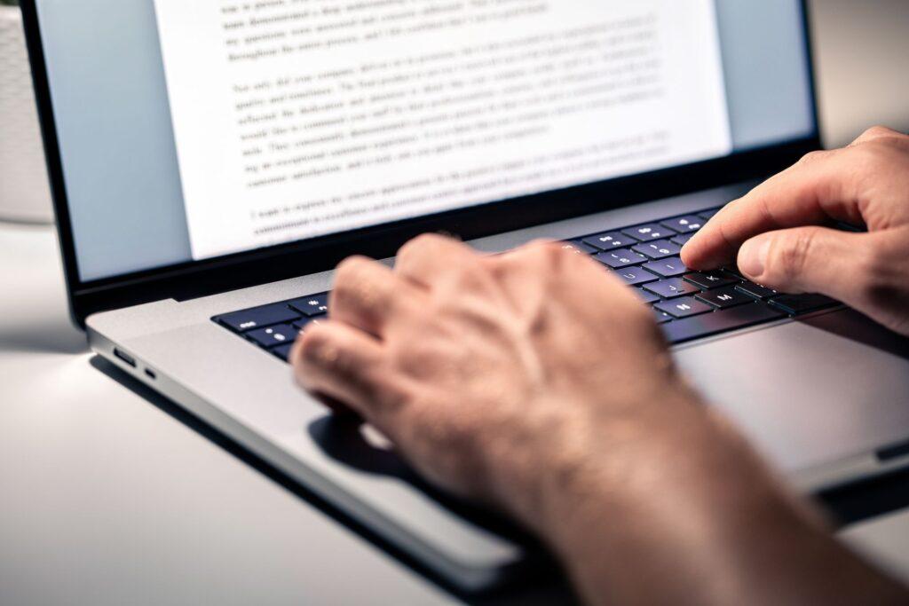 haende schreiben auf laptop mit geoeffnetem textdokument