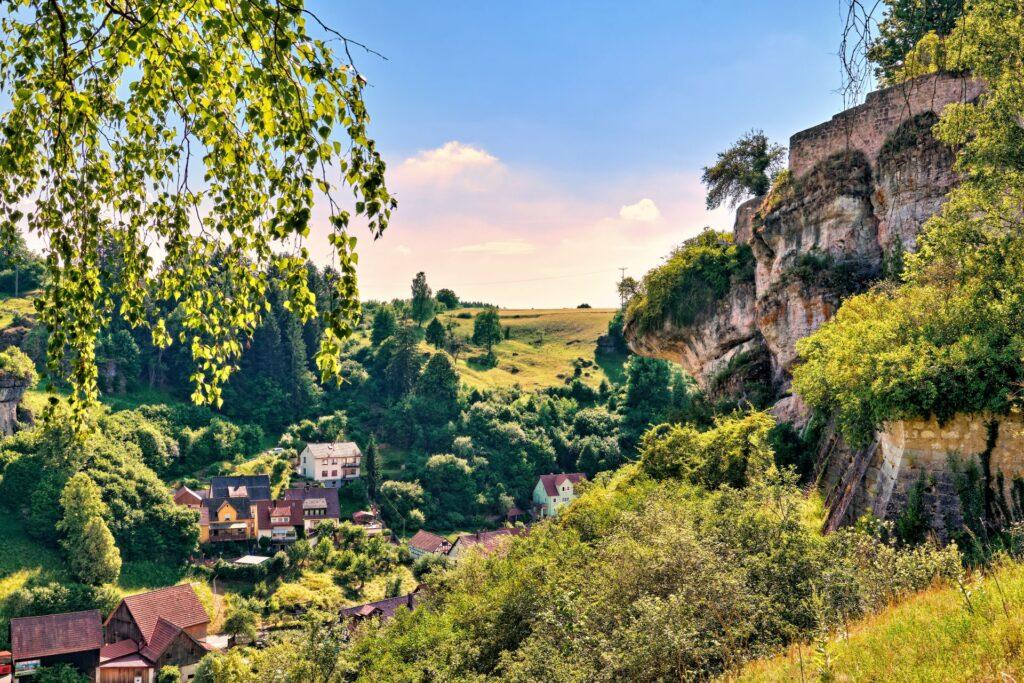 Blick auf ein Dorf in der Fraenkischen Schweiz, umgeben von Felsen, Wäldern und grüner Landschaft im Sommer
