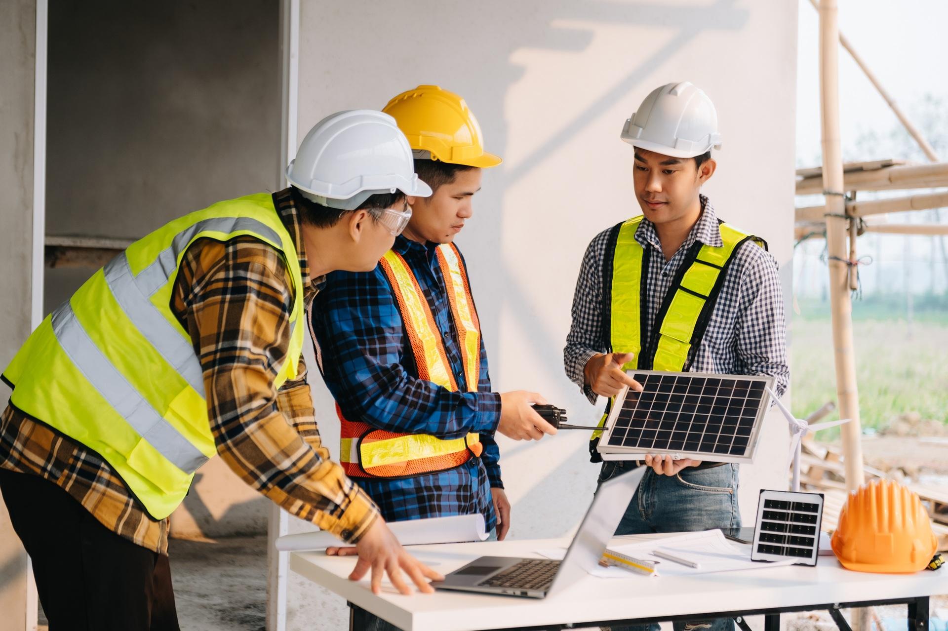 Drei Bauarbeiter prüfen kleines Solarmodul | Sachverständiger Löschanlagen